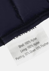 Tummansininen puffer-kangas, jossa on sileä pinta. Siinä on hoito-ohje, joka luettelee materiaalit: päällikangas ja vuori 100 % nylon, täyte 90 % untuvaa, 10 % höyhentä.