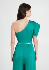 Grünes Satin-Ein-Schulter-Oberteil mit tailliertem Oberteil und Puffärmel. Verkürzte Länge, glatte Textur und minimalistischem Design.