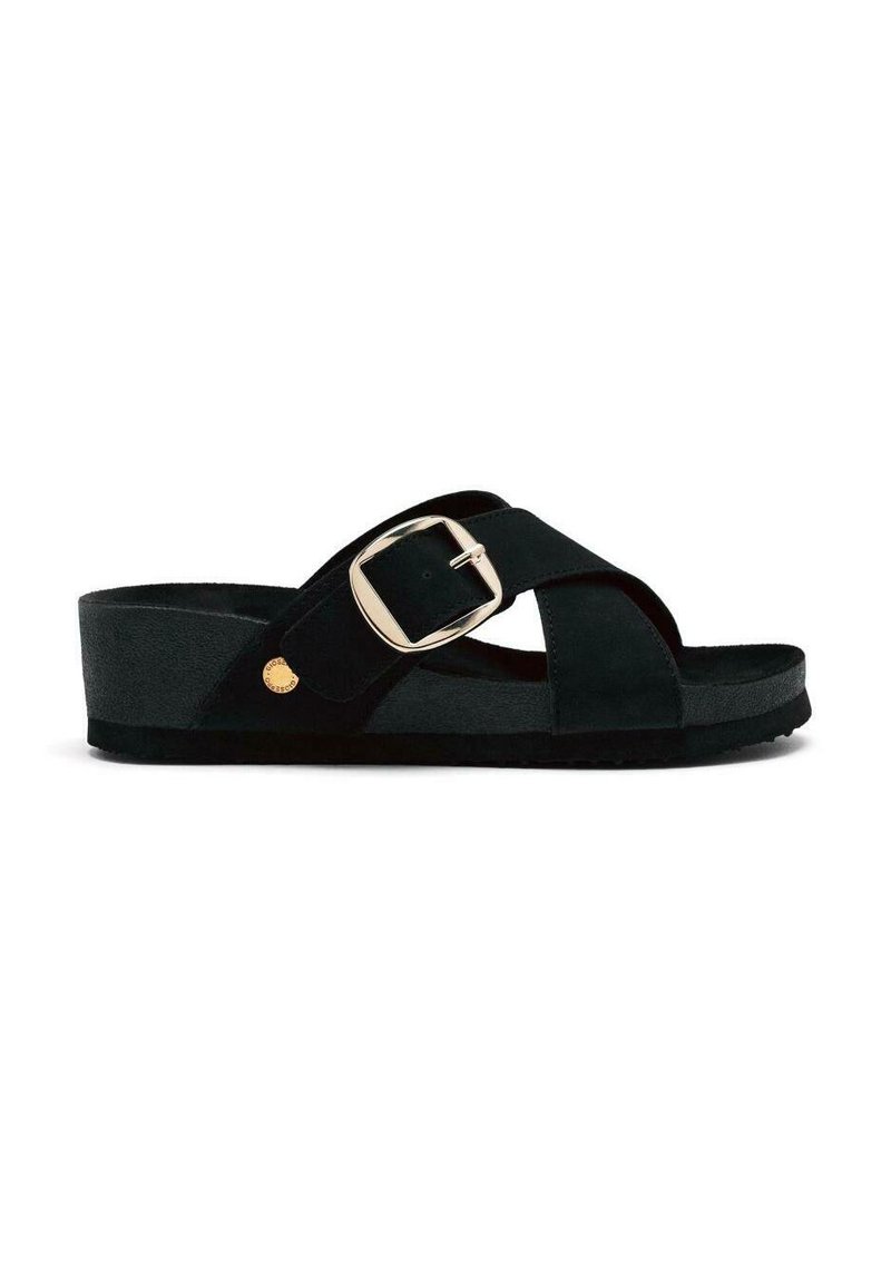 Sandalia de ante negra con diseño de tiras cruzadas, hebilla ajustable y suela plana y texturizada. Presenta un acento dorado redondo en el lado exterior.