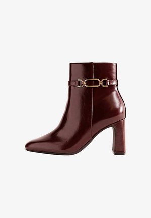 Stivale alla caviglia in pelle sintetica bordeaux con punta affusolata e tacco a blocco. Presenta una fascia decorativa con fibbia in tonalità oro alla caviglia.