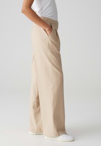 Beige wijde broek gemaakt van lichtgewicht stof, met zijzakken en een schone voorkant met een gladde, op maat gemaakte afwerking.