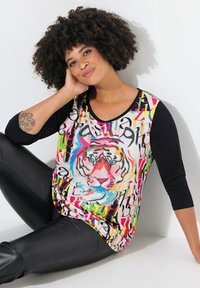 Kleurvol graphic T-shirt met een tijgerontwerp aan de voorkant, met een mix van levendige patronen en zwarte mouwen. Gekozen met zwarte leren legging.
