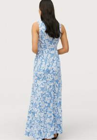 Sininen kukallinen maksimekko, jossa on olkaimeton muotoilu, kerroksellinen helma ja kontrastoivat valkoiset kukkakuviot. Pehmeä kangas.