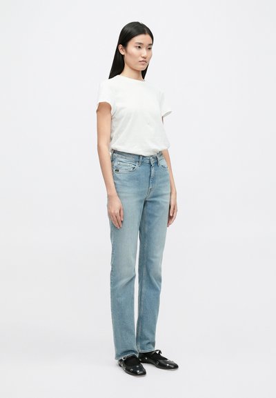 T-shirt branca de manga curta combinada com jeans de denim de perna reta em azul claro. O conjunto apresenta um corte clássico e um design simples e limpo.