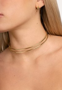 Collana choker in metallo dorato con due bande circolari parallele, texture liscia e un design minimalista. Include anche un piccolo orecchino dorato con un accento.