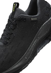 Czarne wodoodporne trampki wykonane z teksturowanej tkaniny, z gładką gumową podeszwą, widocznymi kroplami wody i metką Gore-Tex z boku.