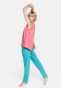 Bez rękawów różowy top z okrągłym dekoltem, połączony z luźnymi tealowymi spodniami. Miękki materiał, luźny krój, prezentujący sportowy, casualowy styl.