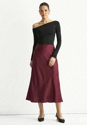 Black long-sleeve top with an off-shoulder design, paired with a flowing burgundy midi skirt. The outfit is complemented by black heeled shoes.
