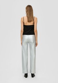 Haut noir à bretelles fines associé à un pantalon large en métal argenté. Le pantalon présente une texture lisse et deux poches arrière.