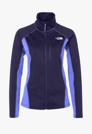 Fleece jacket in donkerpaars met lichtpaarse accenten, met een ritszak en hoge kraag; gecombineerd met zwarte broek en stevige laarzen.