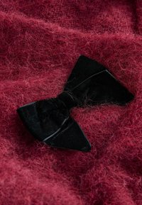 Mustad sametist lips punasel kangal, millel on nähtavad kiud, luues pehme ja mugava materjalide ja värvide kontrasti.