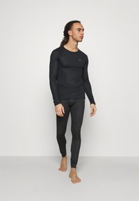 Schwarzes langärmliges Thermoshirt mit enganliegender Passform, kombiniert mit passenden schwarzen Leggings. Beides hat eine glatte Textur und ist leicht.