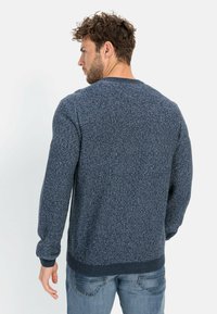 Dunkelblauer Strickpullover mit strukturiertem Muster, Rundhalsausschnitt und rippten Bündchen und Saum, getragen über hellblauen Jeans.