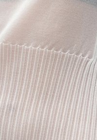 Πλεκτό ύφασμα σε απαλό, ανοιχτό ροζ χρώμα με διακριτές διαγώνιες ρίγες. Έχει υφή με λεία επιφάνεια και λεπτομέρεια με κυματιστό τελείωμα στην κορυφή.