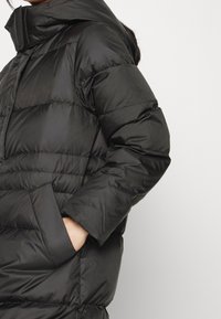 Chaqueta acolchada negra con capucha, que presenta secciones acolchadas horizontales, bolsillos frontales y una textura suave y brillante.