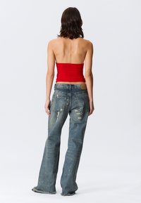 Raudonas, be petnešėlių palaidinė su surinkta tekstūra, derinama su šviesiai mėlynais plačiomis kojomis, pažeistais džinsais, turinčiais plyšimų ir nusitrynusius galus, matoma iš nugaros.