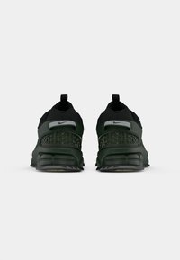 Baskets Nike en vert foncé et noir, dotées d'une tige en mesh, d'un talon texturé et d'un rembourrage visible, avec une semelle en caoutchouc durable.