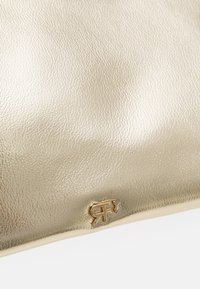 Surface en cuir doré brillant avec un petit logo doré embossé présentant des lettres stylisées près du bord inférieur.
