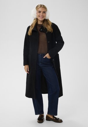 Juodas vilnonis paltas su tekstūruotu paviršiumi, turintis vieną mygtukų eilę, derinamas su rudu megztiniu ir mėlynomis džinsais. Baltos dirbtinės kailio ausinės.