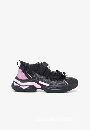 Pantof sport negru și roz cu talpă groasă, margine plisată, curea cu Velcro și detaliu de cusătură albă, prezentat în profil lateral pe fundal alb.