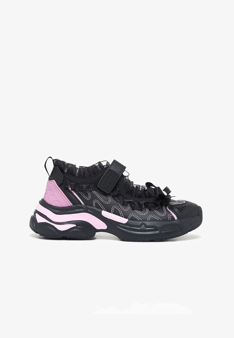 Zwarte en roze sneaker met dikke zool, gerimpelde rand, klittenbandriem en witte stiksel details, zijaanzicht op witte achtergrond.