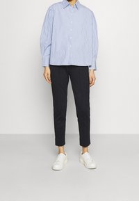 Light blue and white striped button-up shirt with puffed sleeves, paired with tailored dark gray pants and white sneakers.