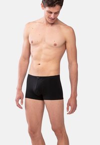 Boxers noirs sur un mannequin masculin, avec une coupe ajustée, une texture douce et un logo sur la taille, conçus pour le confort et le soutien.