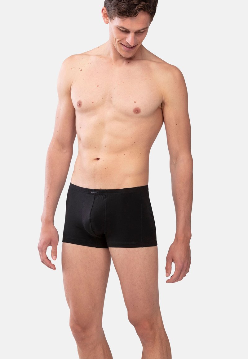 Boxers noirs sur un mannequin masculin, avec une coupe ajustée, une texture douce et un logo sur la taille, conçus pour le confort et le soutien.