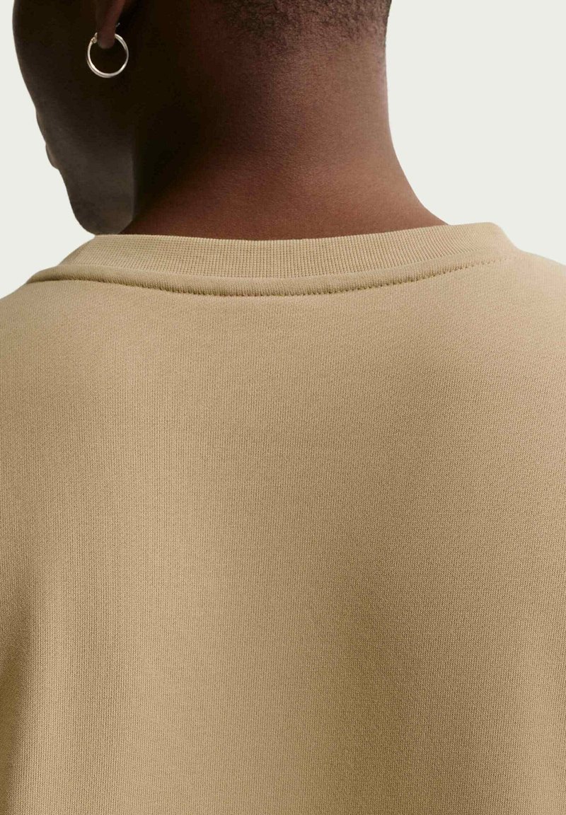Vista posteriore di una persona che indossa una camicia beige, con capelli corti e un orecchino a cerchio d'argento all'orecchio sinistro.