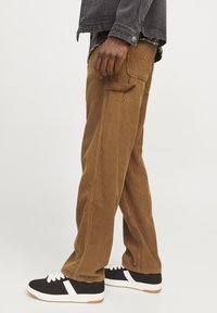 Brown corduroy pants with a relaxed fit, side pockets, and visible texture paired with black and white sneakers featuring a gum sole.
