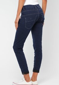 Mörkblå smala jeans i denim med texturerad yta, med bakfickor, uppvikta fållar och kontrasterande sömmar.