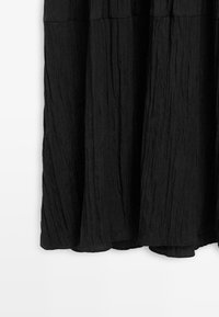 Langer schwarzer Rock mit strukturierter, gekräuselter Stoffstruktur und gerafftem Bund, hängt vor einem schlichten weißen Hintergrund.