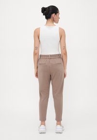 Pantalons marron à taille élastique avec poches latérales, design de jambe fuselée et texture lisse, associés à un haut sans manches blanc.