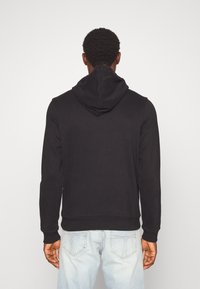 Musta huppari, jossa on kengurutasku, resorit hihansuissa ja helmassa, valmistettu teksturoidusta puuvillakankaasta, esitetty takaa.