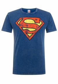 Blue cotton t-shirt featuring a large, worn-looking Superman emblem in yellow, red, and orange, with short sleeves and a crew neckline.