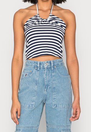 Kobieta ubrana w granatowo-biały, paskowany, krótkotrwały top typu halter oraz jasnoniebieskie dżinsy z wysokim stanem i dużymi przednimi kieszeniami.