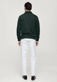 Green knit pullover with a collared neck, paired with white tapered trousers and black shoes. The fabric has a textured finish.