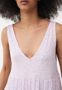 Ärmelloses Kleid aus leichtem Stoff mit lilafarbener Basis, weißem Blumenmuster und tiefem V-Ausschnitt. Weiche Textur mit fließender Form.