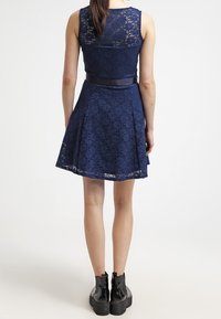 Robe en dentelle bleu marine avec un corsage ajusté, une jupe évasée et une ceinture en satin. Présente des motifs en dentelle délicats et une silhouette en A flatteuse.