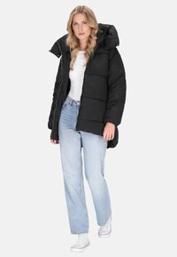 Sort puffervindjakke med hætte, med lynlåslukning, quiltet design og lange ærmer, parret med lyseblå jeans og hvide sneakers.