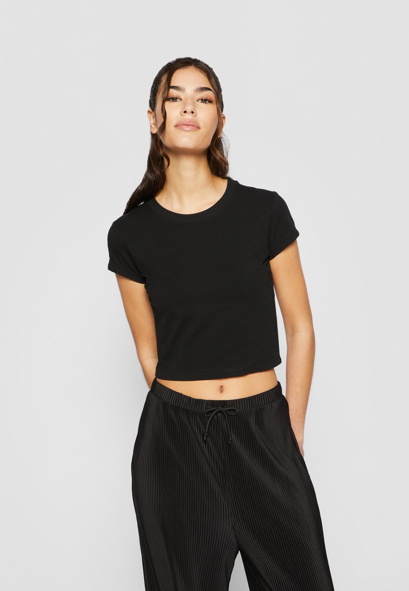 Čierny bavlnený crop top s okrúhlym výstrihom a krátkymi rukávmi, skombinovaný s čiernymi pletenými nohavicami na šnúrku. Jednoduchý dizajn, bez viditeľných vzorov.