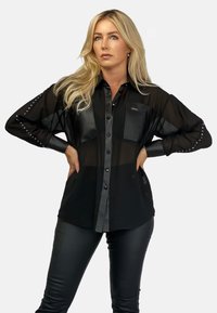 Czarna koszula na guziki z przezroczystym materiałem i skórzanymi detalami, z ozdobnymi ćwiekami na rękawach. W zestawie z czarnymi skórzanymi spodniami.