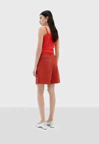 Débardeur côtelé rouge associé à un short couleur rouille. La tenue présente un design ajusté, une texture lisse et des chaussures argentées brillantes.