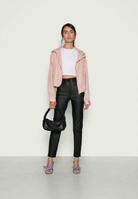 Sweatshirt rosa claro com fecho, top branco curto, calças pretas de imitação de pele, bolsa trançada preta e chinelos com padrão xadrez.