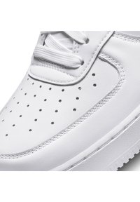 Närbild av en vit lädersneaker med perforeringar, vita snören och detaljerad sömnad på tån och sidan.