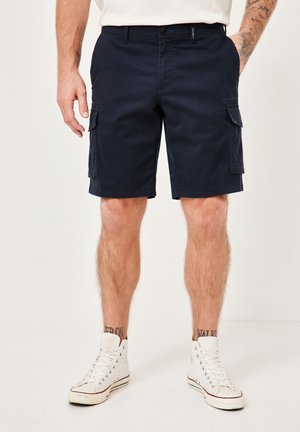 Navy cargo shorts with a sturdy fabric, featuring side pockets, a button closure, and a relaxed fit, paired with white high-top sneakers.
