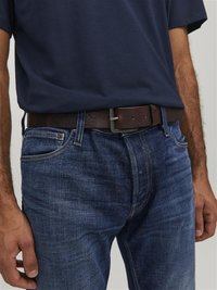 Donkerblauwe t-shirt gecombineerd met blauwe denim jeans. Een bruine leren riem heeft een eenvoudige metalen gesp. De textuur vertoont lichte vervagingdetails.