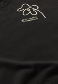 Zwarte sweatshirt met een wit geborduurd bloemenontwerp en de tekst "MAAK EEN TUIN door THINKING MU" in een eenvoudige, strakke lettertype.