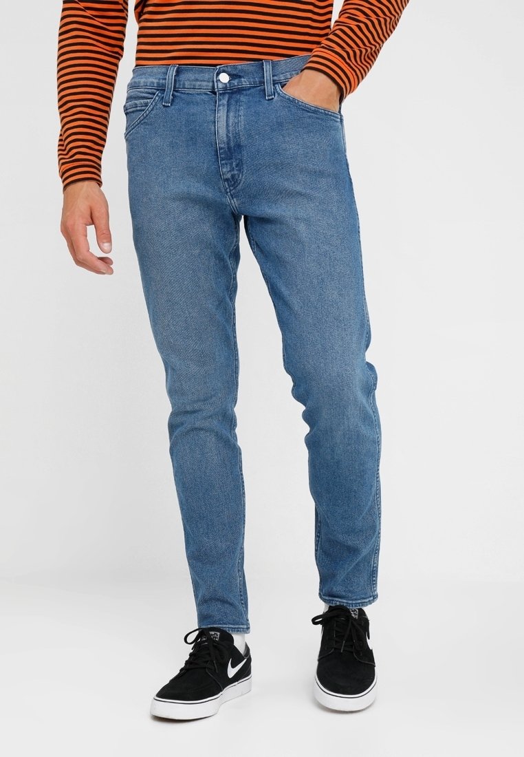 Blå denimjeans med slim fit och fem fickor. Har en enda knappstängning och lätt blekning. Bärs med svarta sneakers.