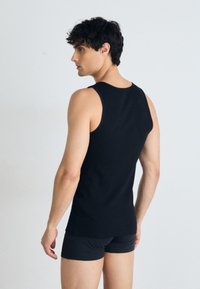 Débardeur noir sans manches en tissu lisse, avec un col rond et un design ajusté, porté avec un short noir.